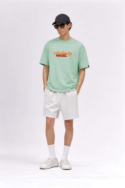 Person wearing a light green t-shirt with text, white shorts, white sneakers, and a black cap on a white background