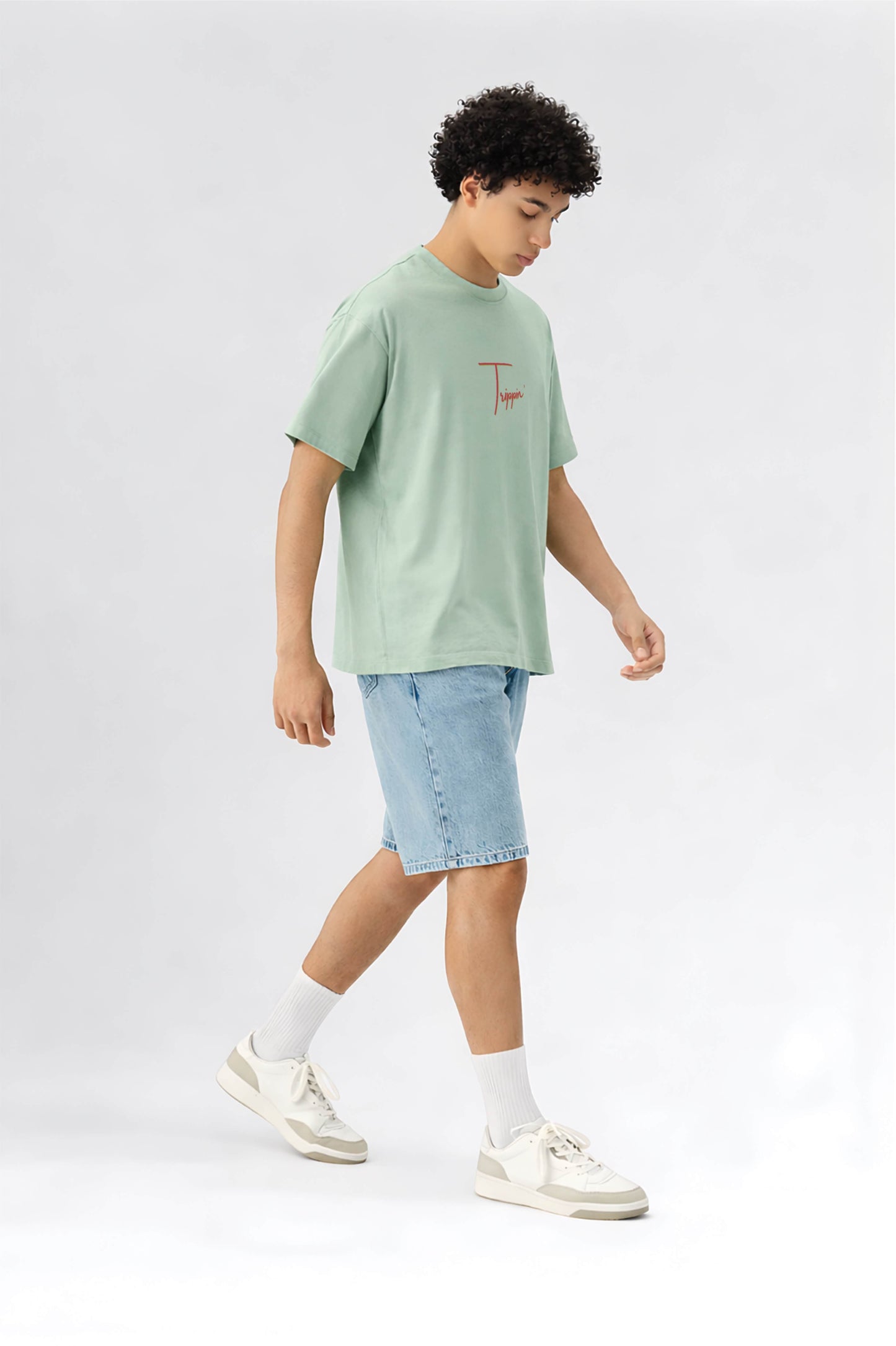 Person wearing a light green t-shirt and denim shorts on a white background
