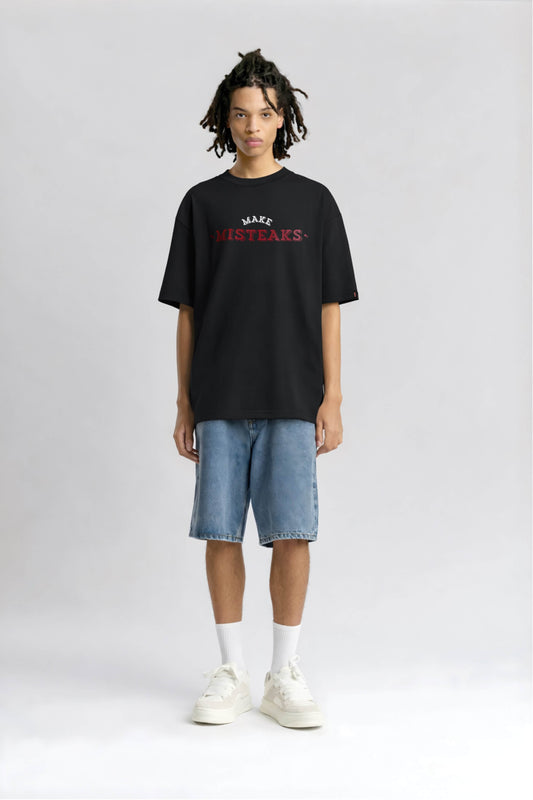 Person wearing a black t-shirt with text and light blue shorts on a white background
