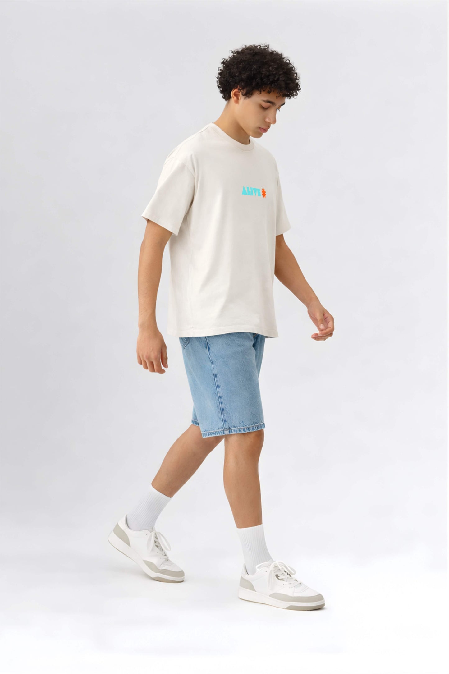 Person wearing an off-white t-shirt with a logo and light blue shorts on a white background