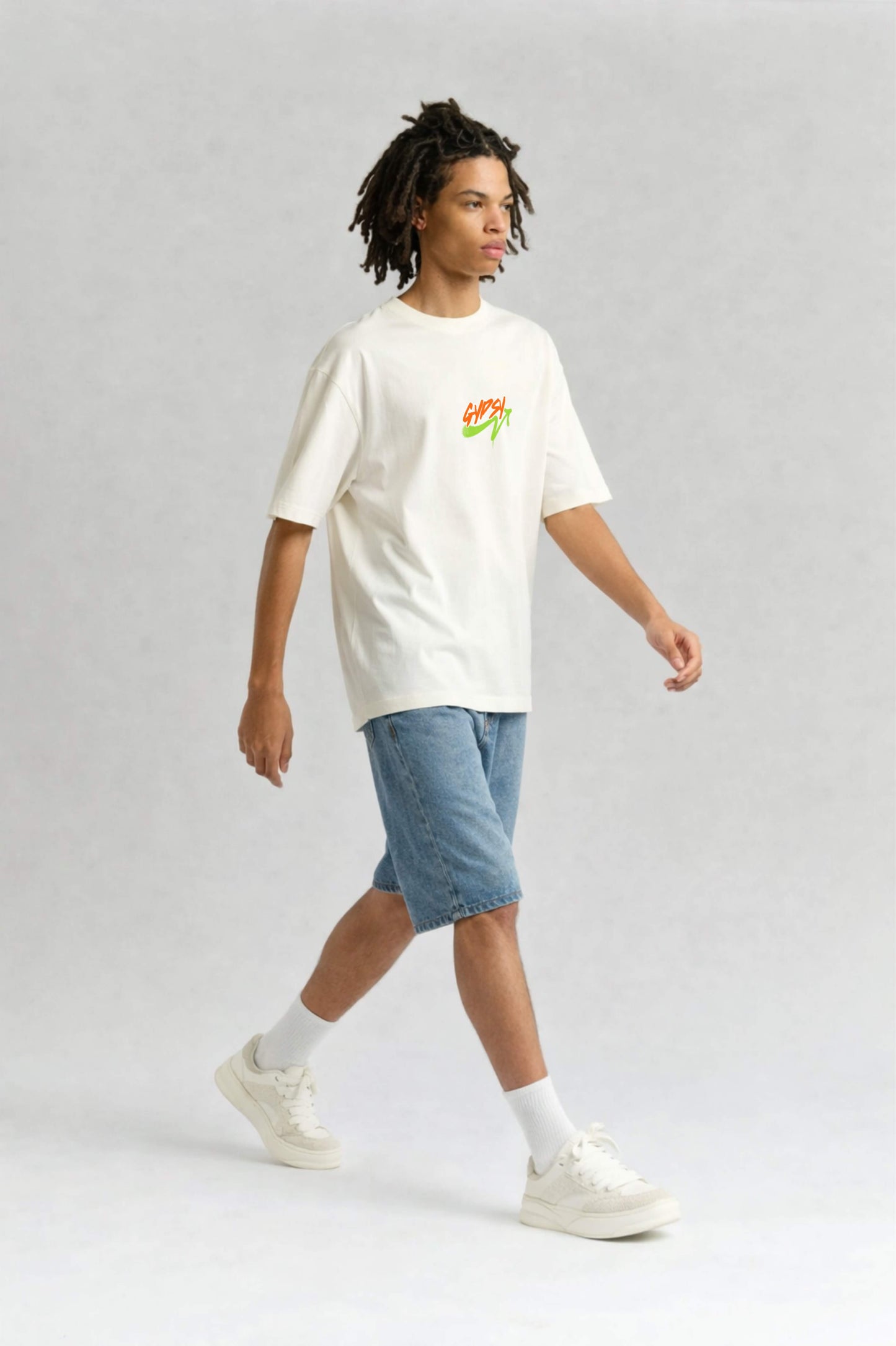 Person wearing an offwhite t-shirt with a colorful design and blue shorts on a light gray background