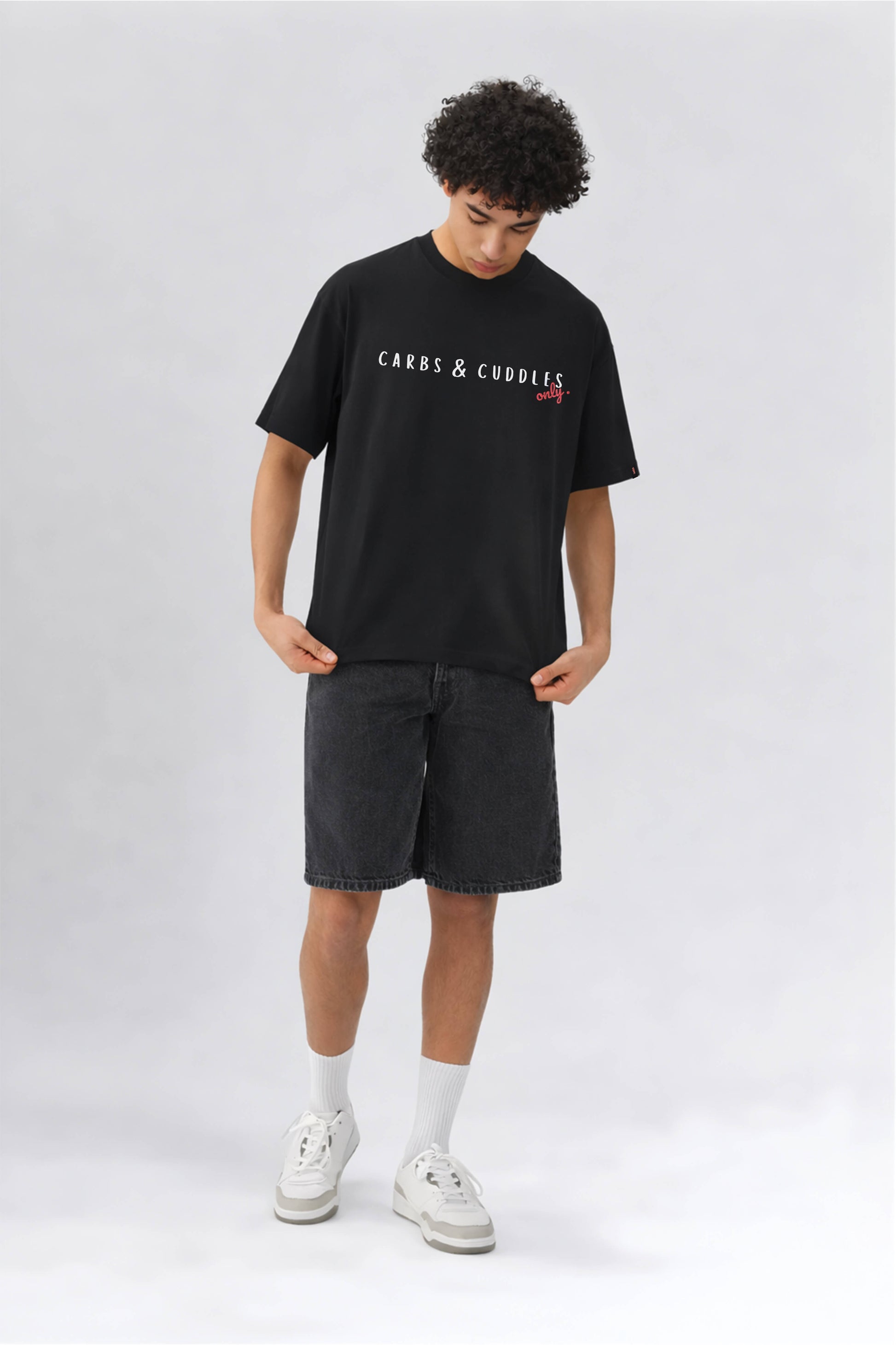 Person wearing a black t-shirt with text and dark shorts on a white background