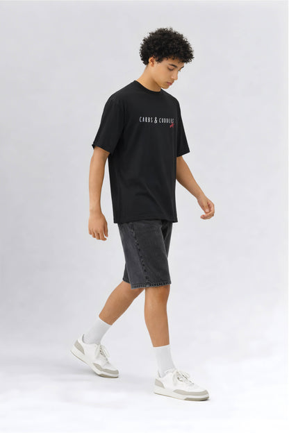 Person wearing a black t-shirt with branding and gray shorts on a white background