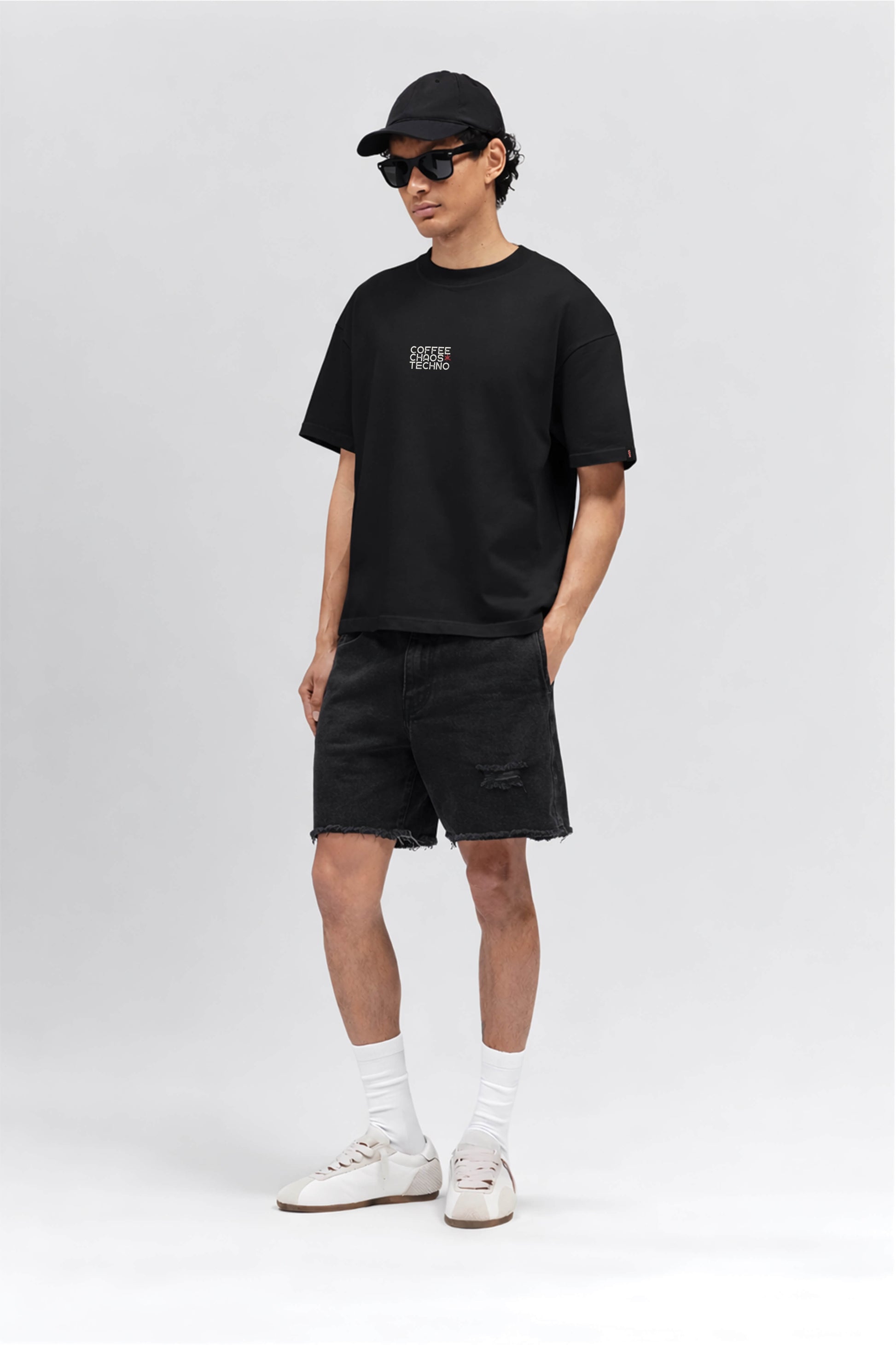 Person wearing a black t-shirt with a logo, black shorts, white socks, and sneakers on a white background