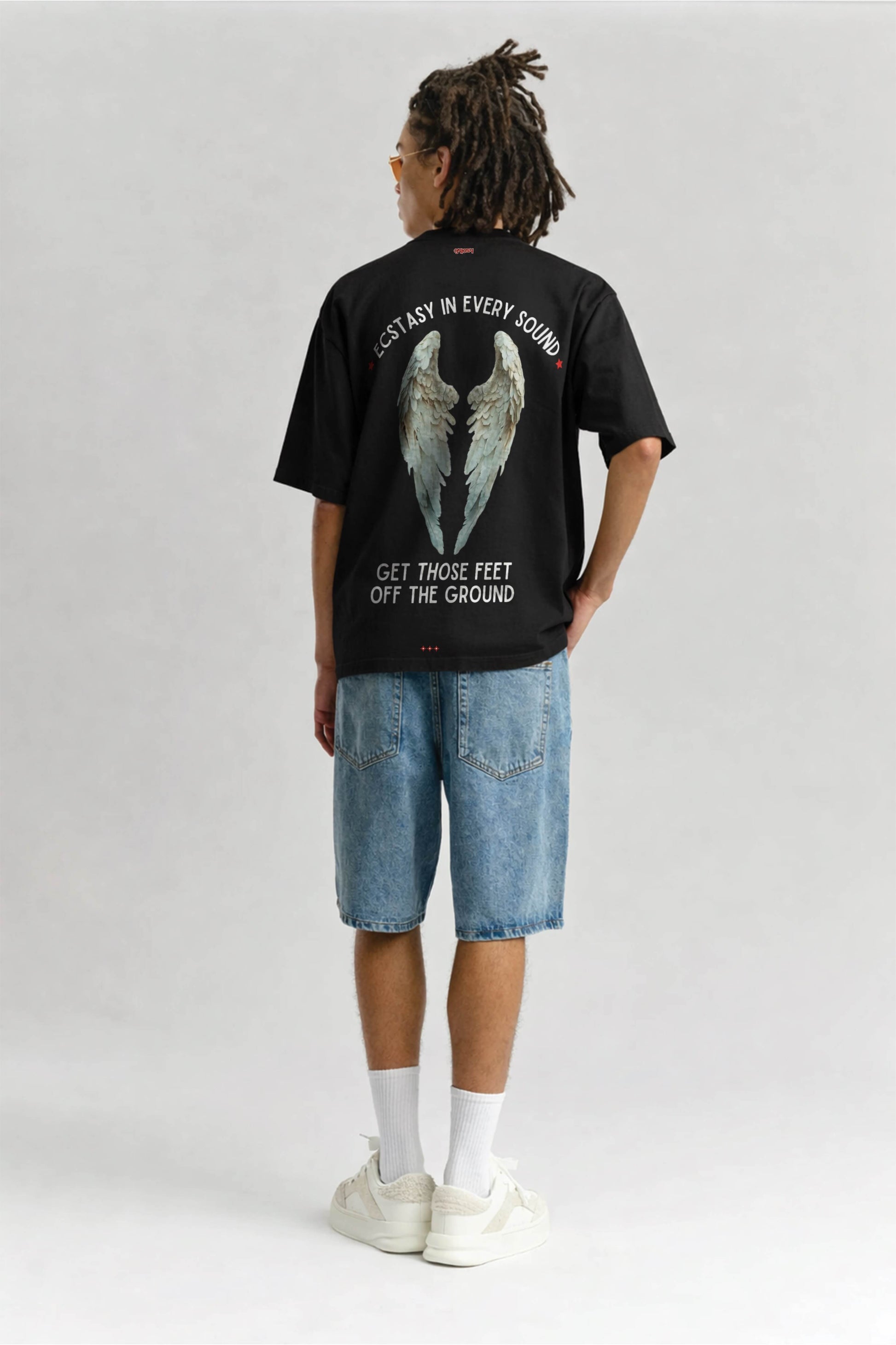 Person wearing a black t-shirt with angel wings graphic and text on a plain background