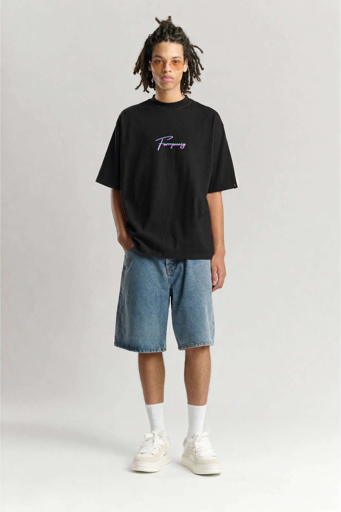 Person wearing a black t-shirt with text, blue shorts, and white sneakers on a light gray background
