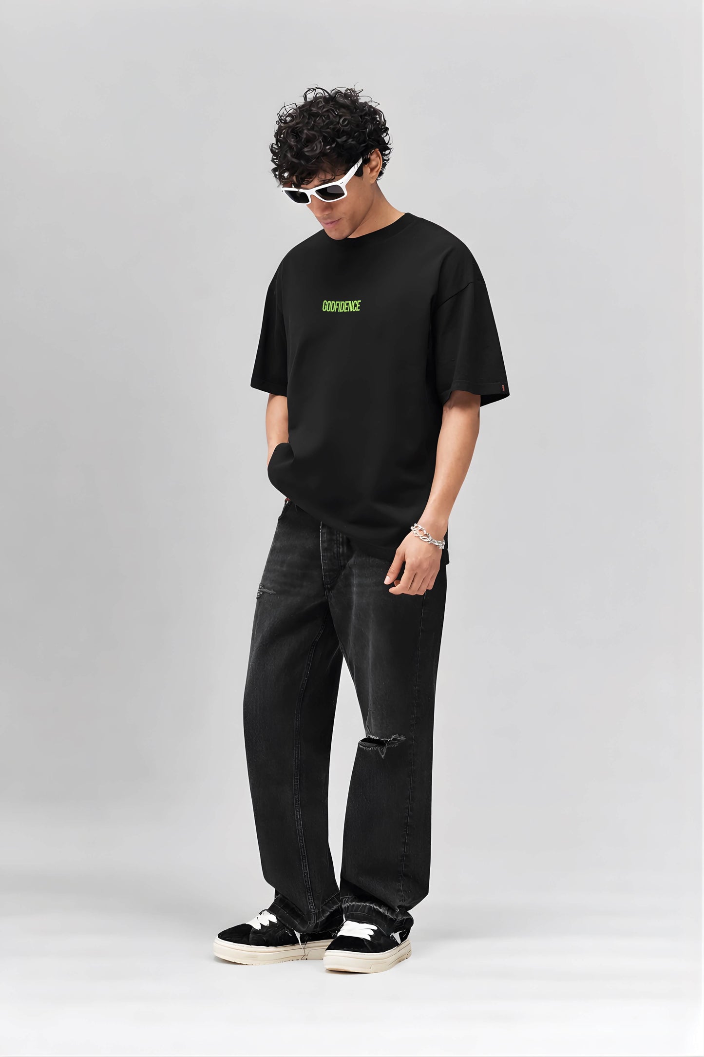Person wearing a black t-shirt with green text and dark jeans on a white background