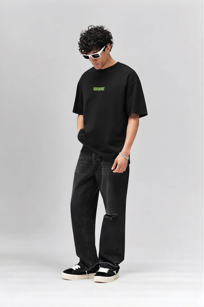 Person wearing a black t-shirt with green text and dark jeans on a white background
