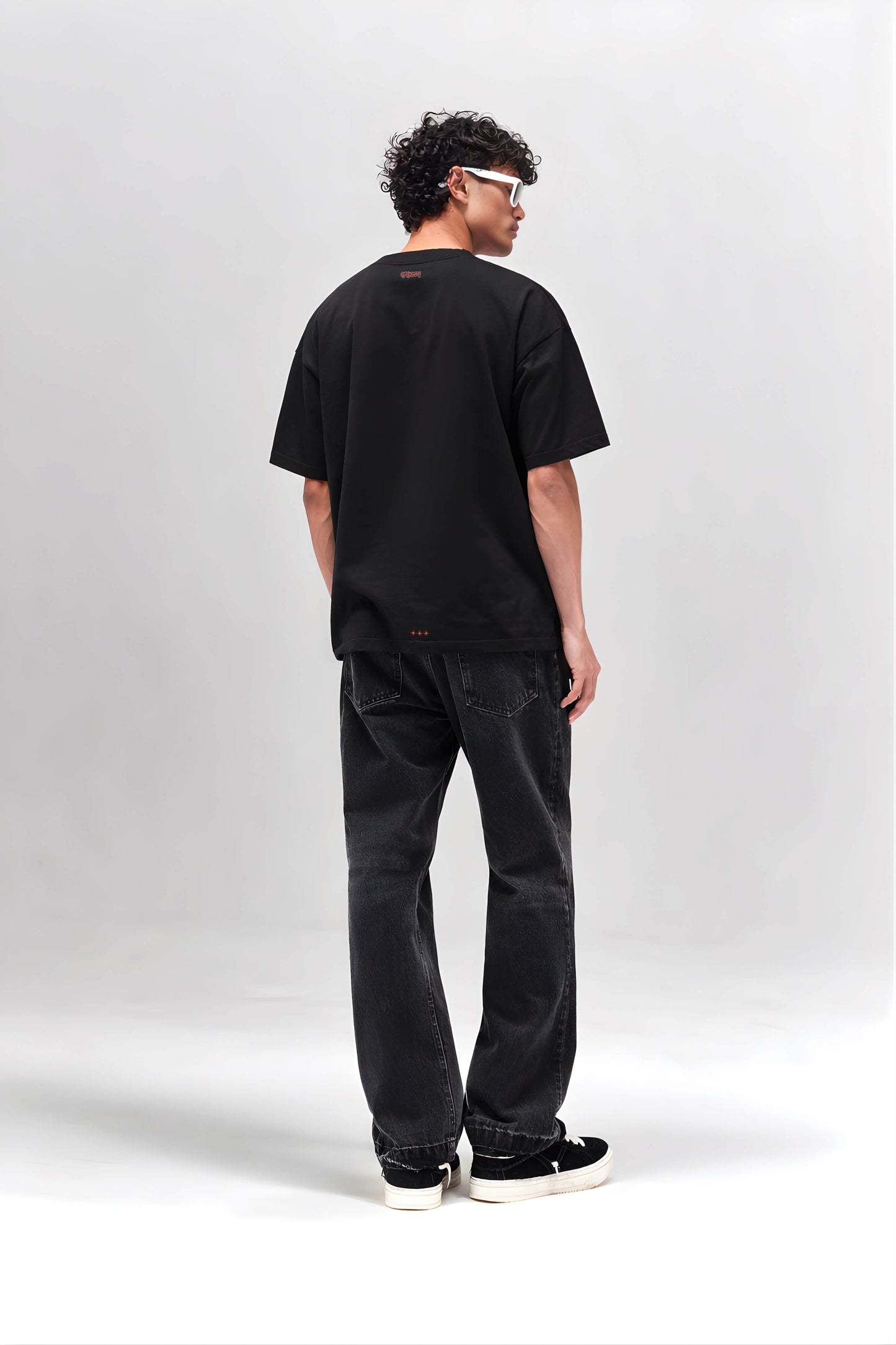 Person wearing a black t-shirt and jeans standing against a white background