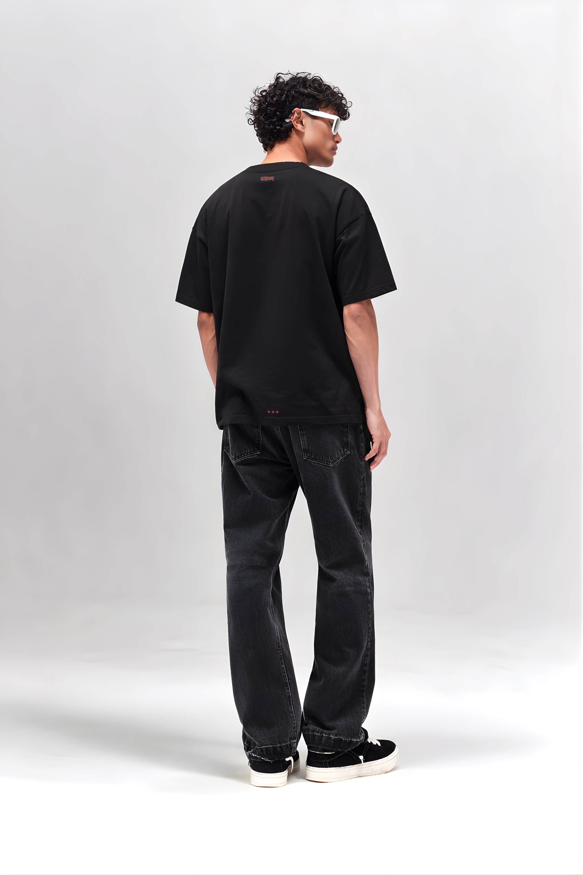 Person wearing a black t-shirt and jeans standing against a white background