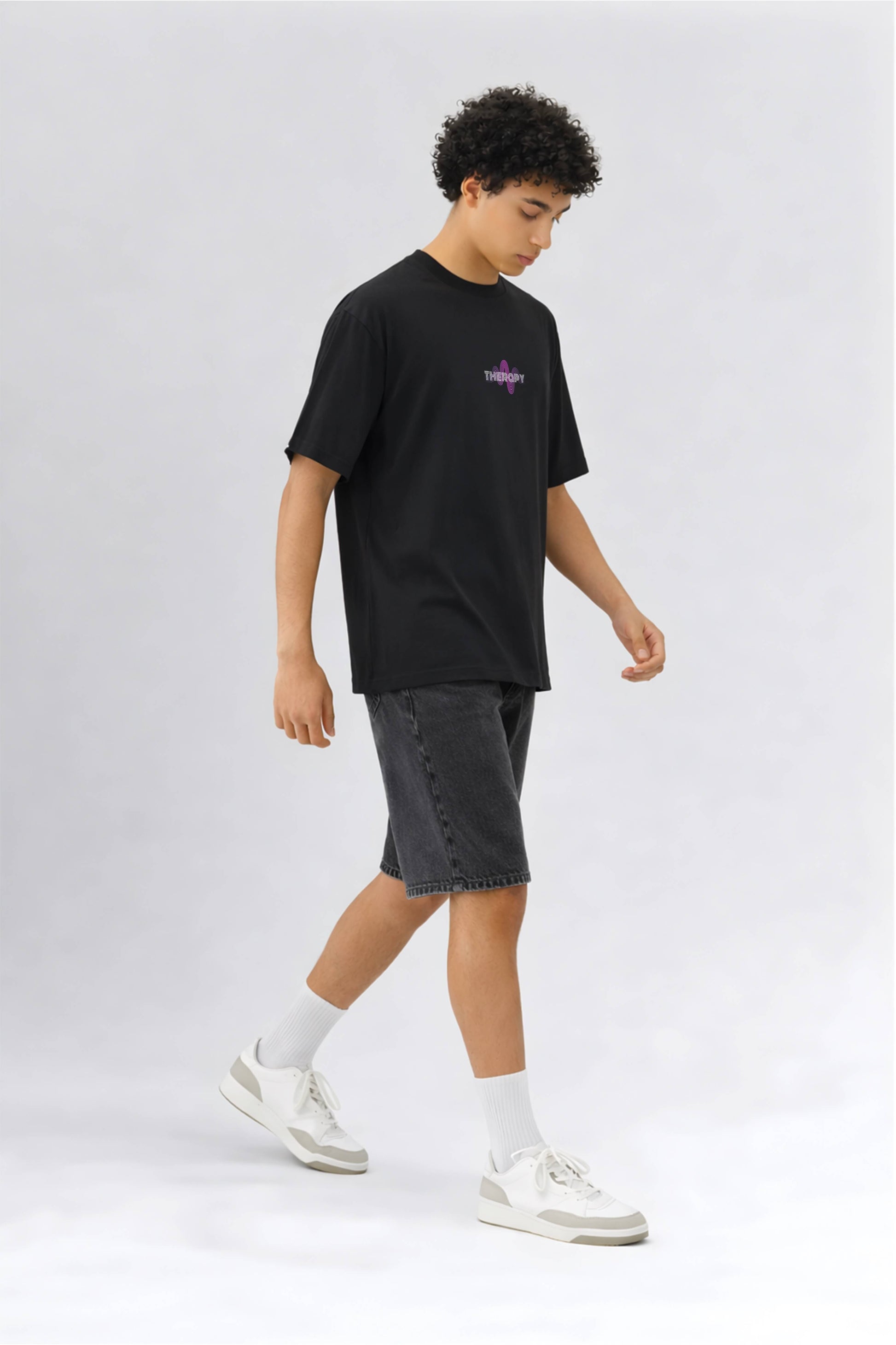 Person wearing a black t-shirt with branding and gray shorts on a white background