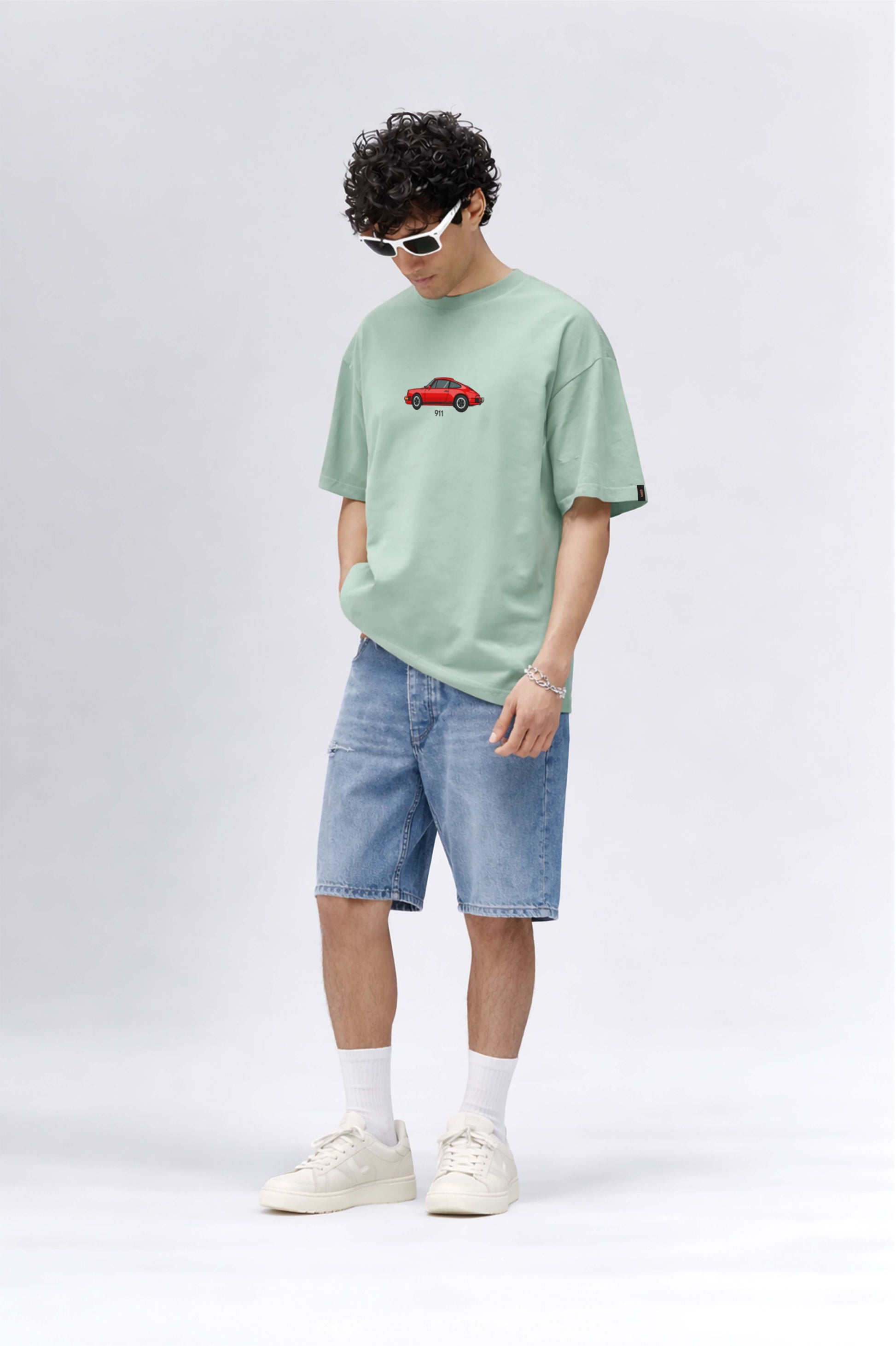 Person wearing a light green t-shirt with a red car graphic and blue shorts on a white background