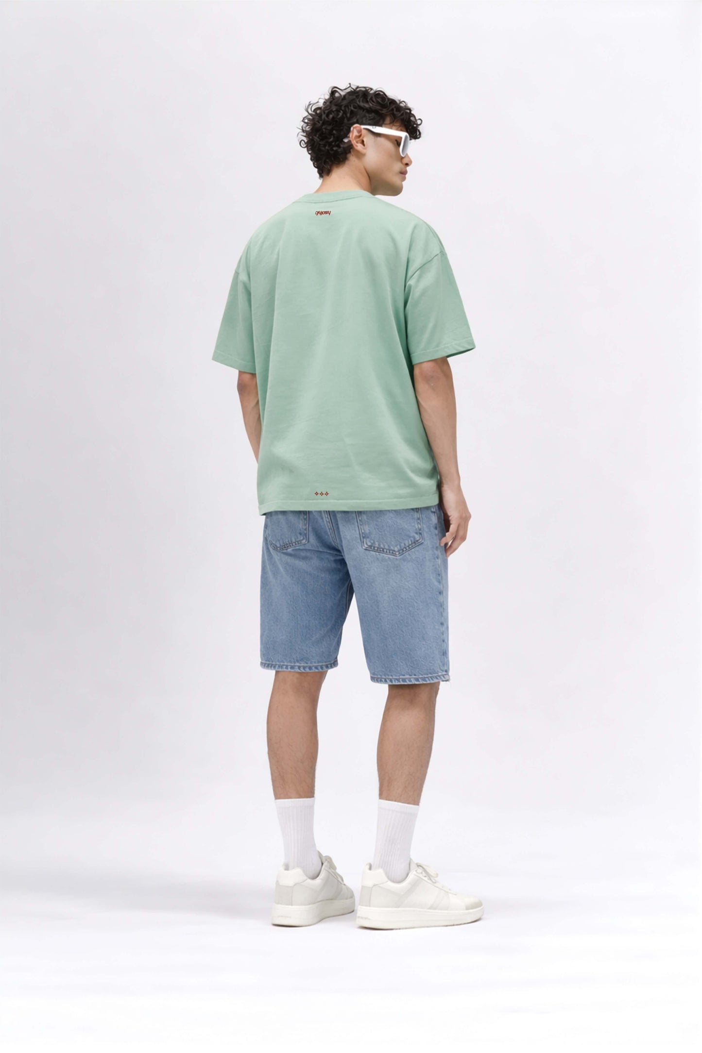 Man wearing a green t-shirt and blue shorts on a white background