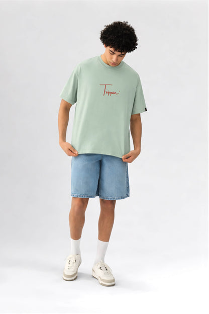 Person wearing a light green t-shirt with a logo and blue shorts on a white background