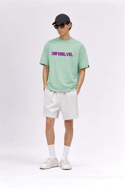 Person wearing a light green t-shirt with text, white shorts, white sneakers, and a black cap on a white background