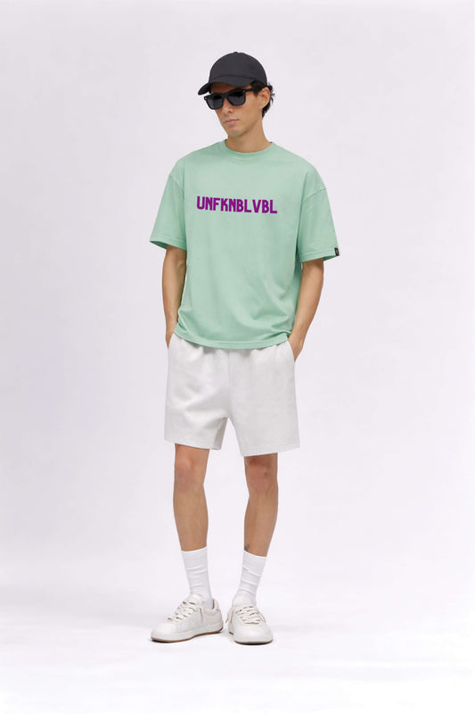 Person wearing a light green t-shirt with text, white shorts, white sneakers, and a black cap on a white background