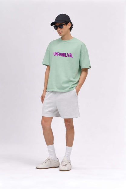 Person wearing a light green t-shirt with text, white shorts, and a black cap on a white background