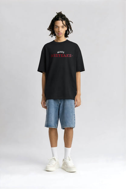 Person wearing a black t-shirt with text and light blue shorts on a white background