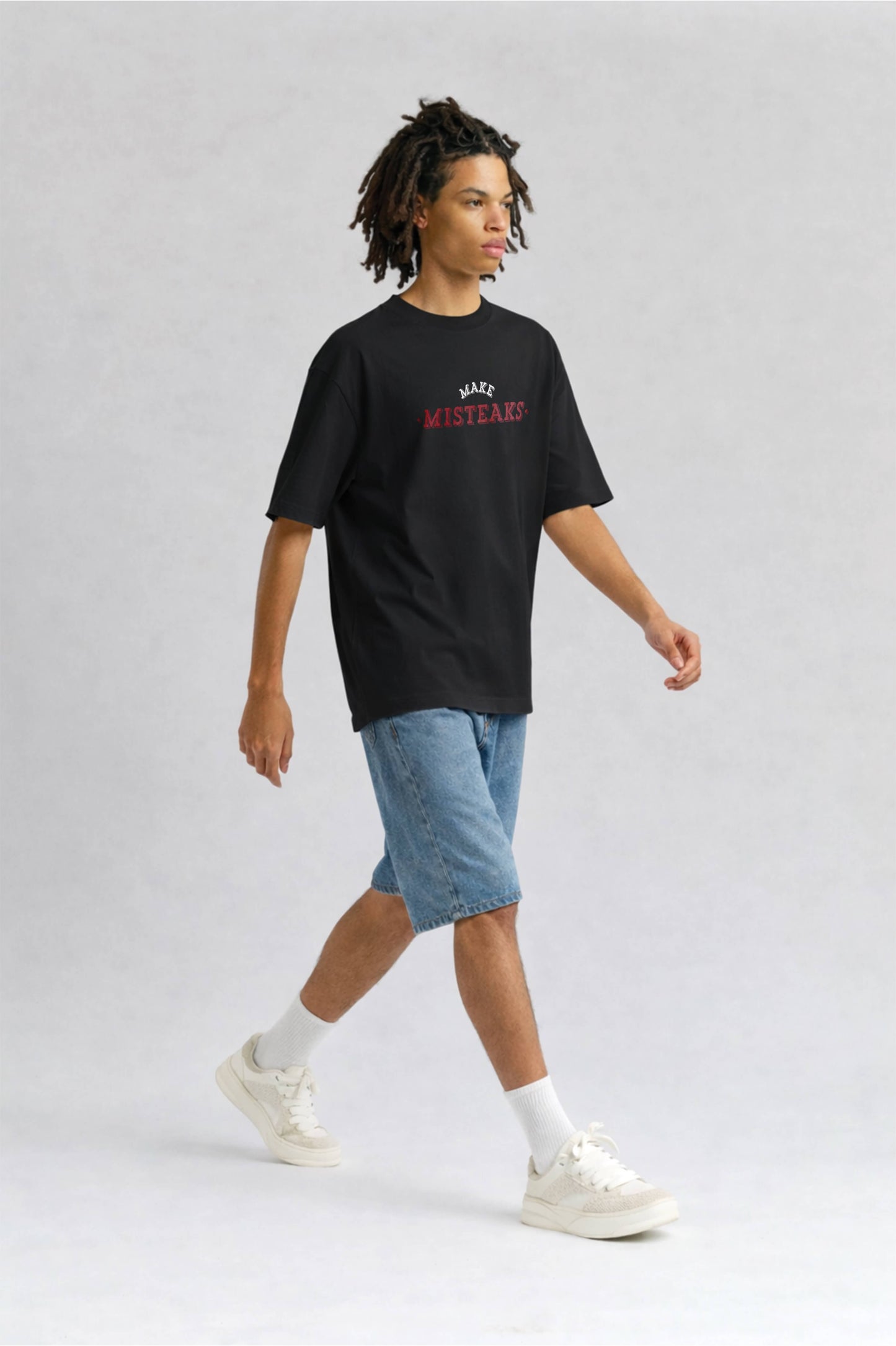 Person wearing a black t-shirt with red text and denim shorts on a light gray background