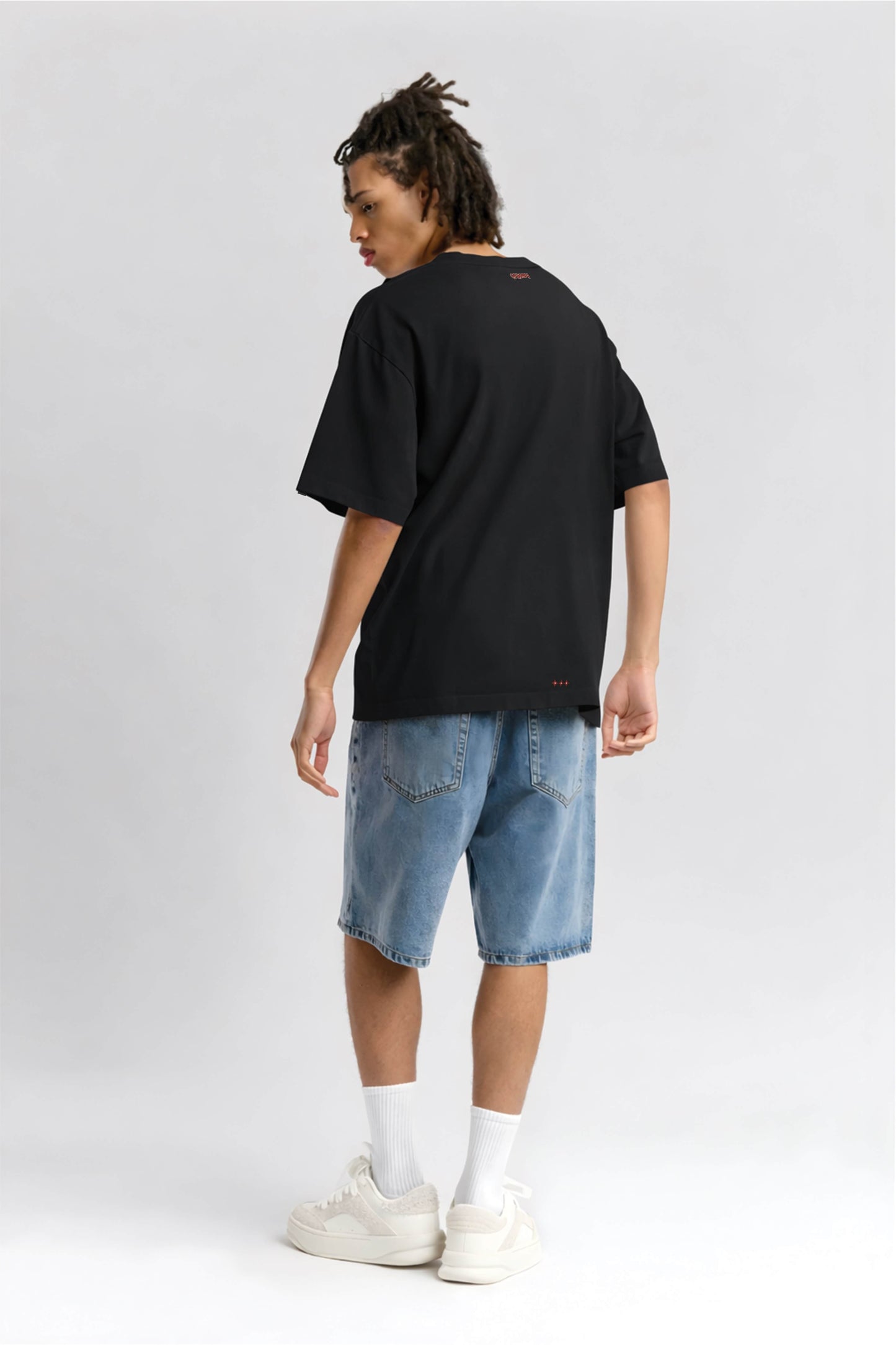 Person wearing a black t-shirt and blue denim shorts on a white background