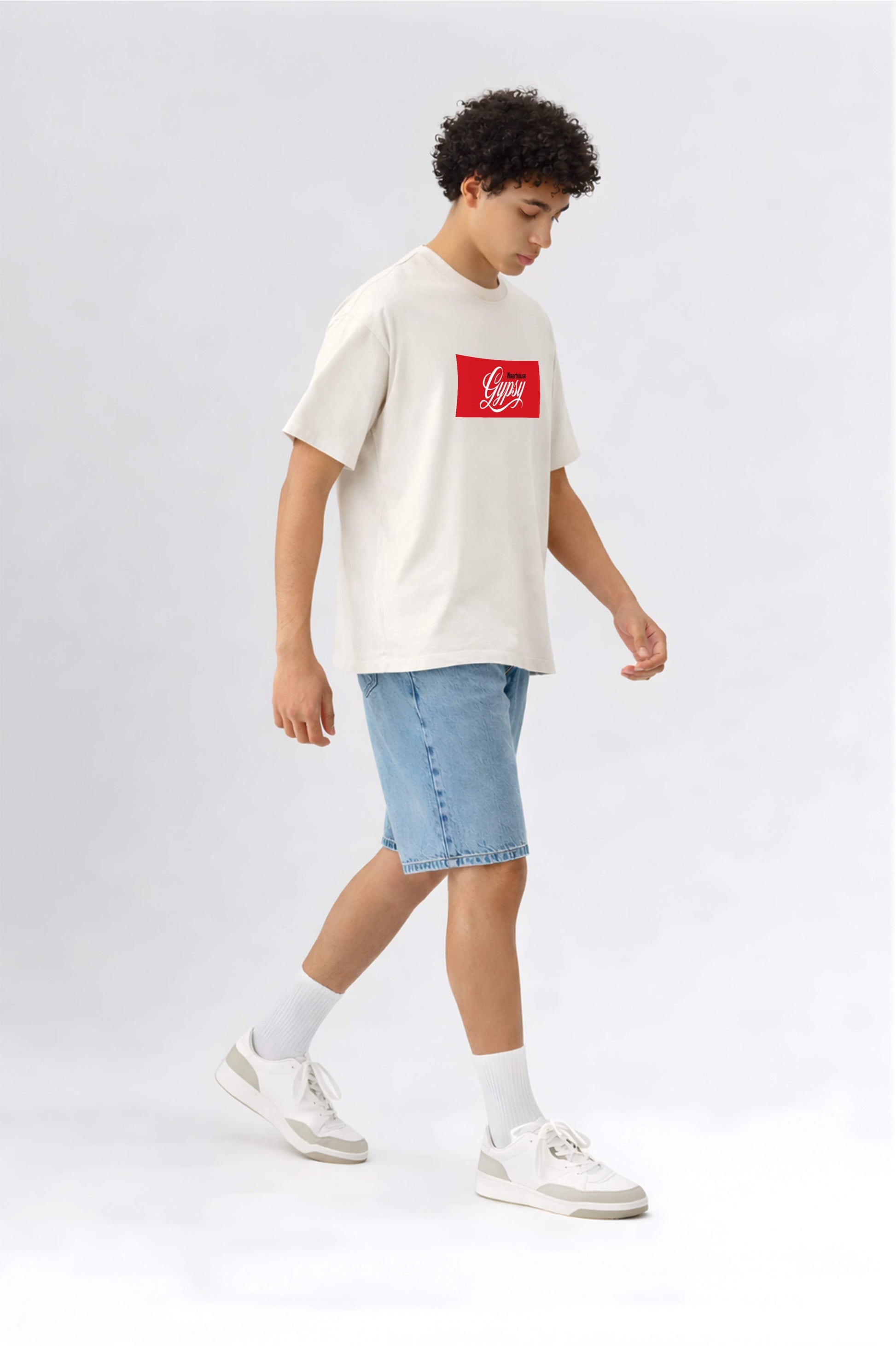 Person wearing a white t-shirt with a red logo and blue shorts on a light gray background