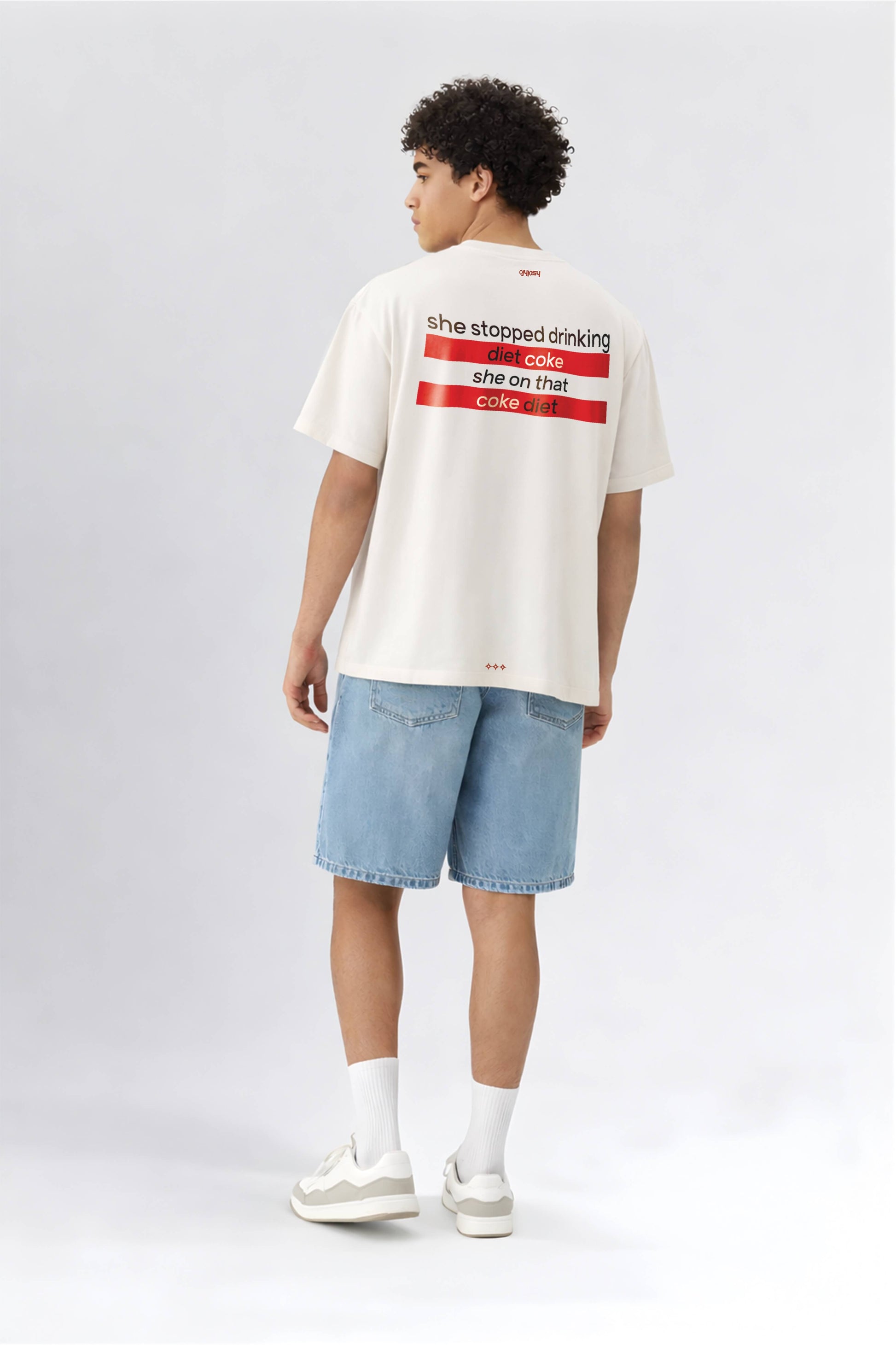Person wearing a white t-shirt with text on the back, standing against a plain background