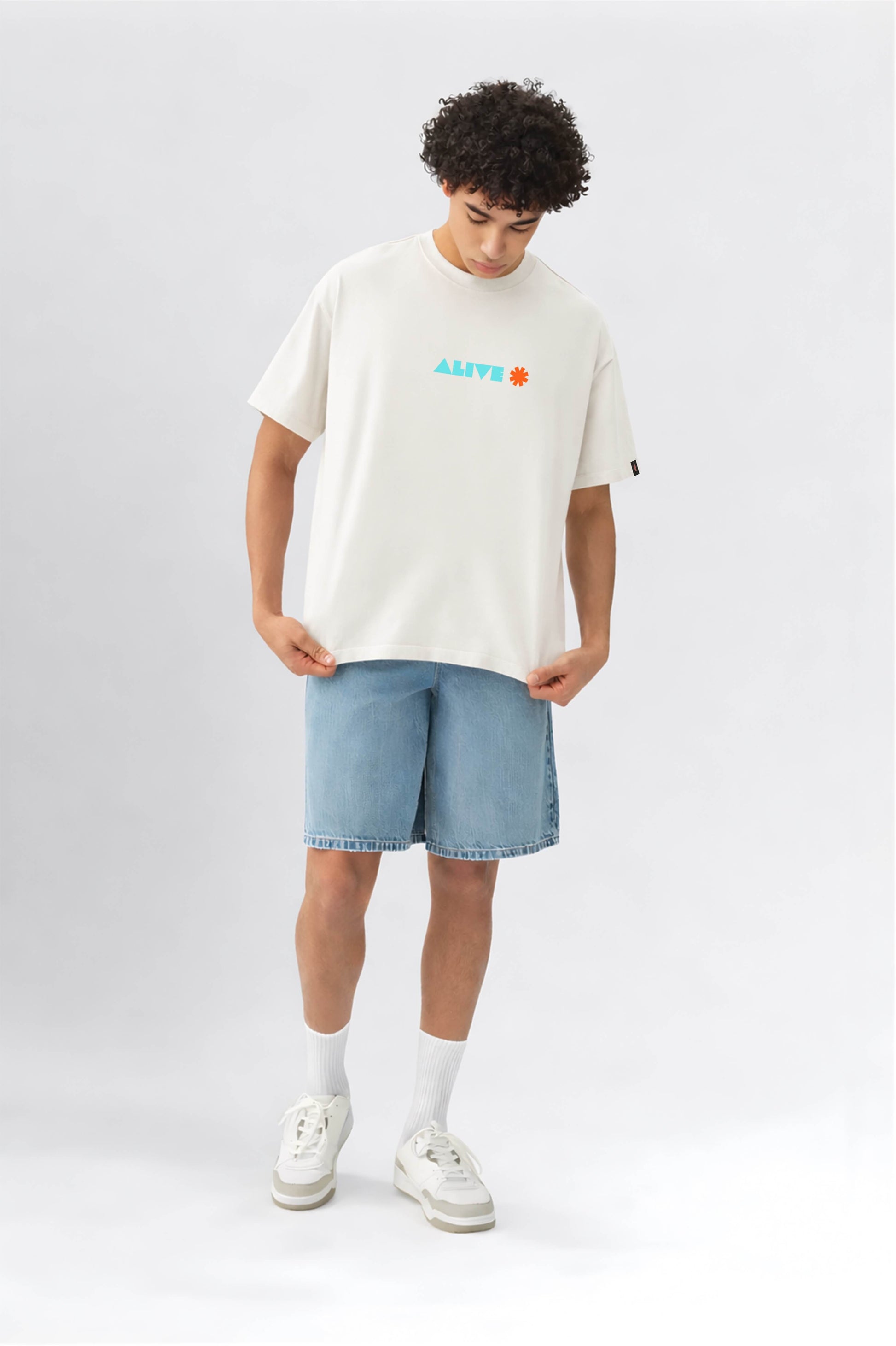 Person wearing an offwhite t-shirt with colorful text and light blue shorts on a white background
