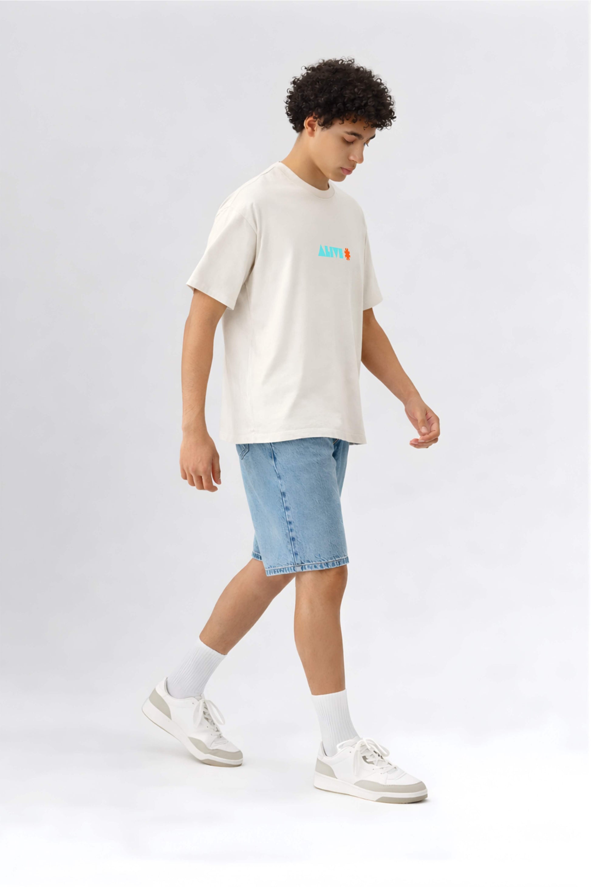 Person wearing an off-white t-shirt with a logo and light blue shorts on a white background