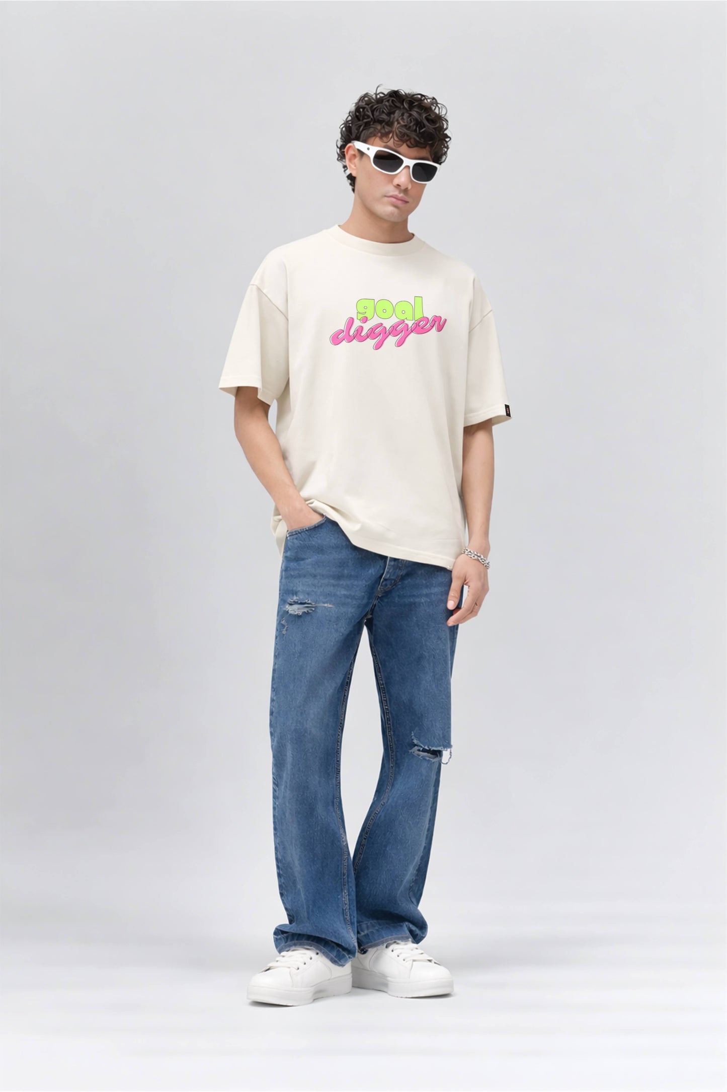 Person wearing an off white t-shirt with colorful text and blue jeans on a gray background