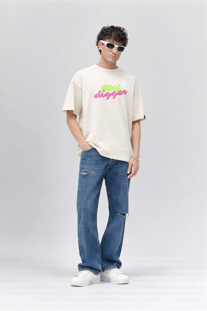 Person wearing an off white t-shirt with colorful text and blue jeans on a gray background