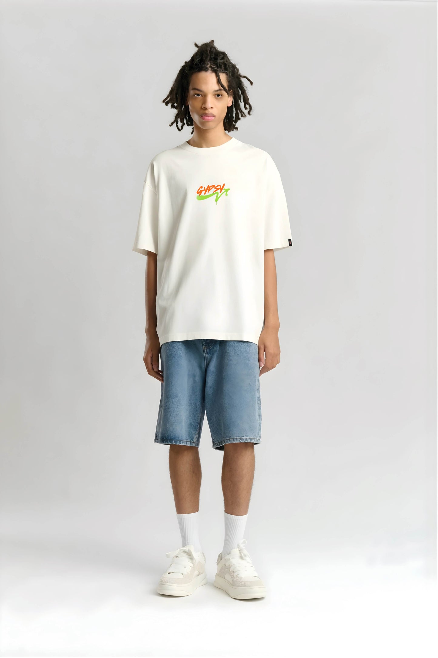 Person wearing a white t-shirt with a colorful logo and blue shorts on a light gray background