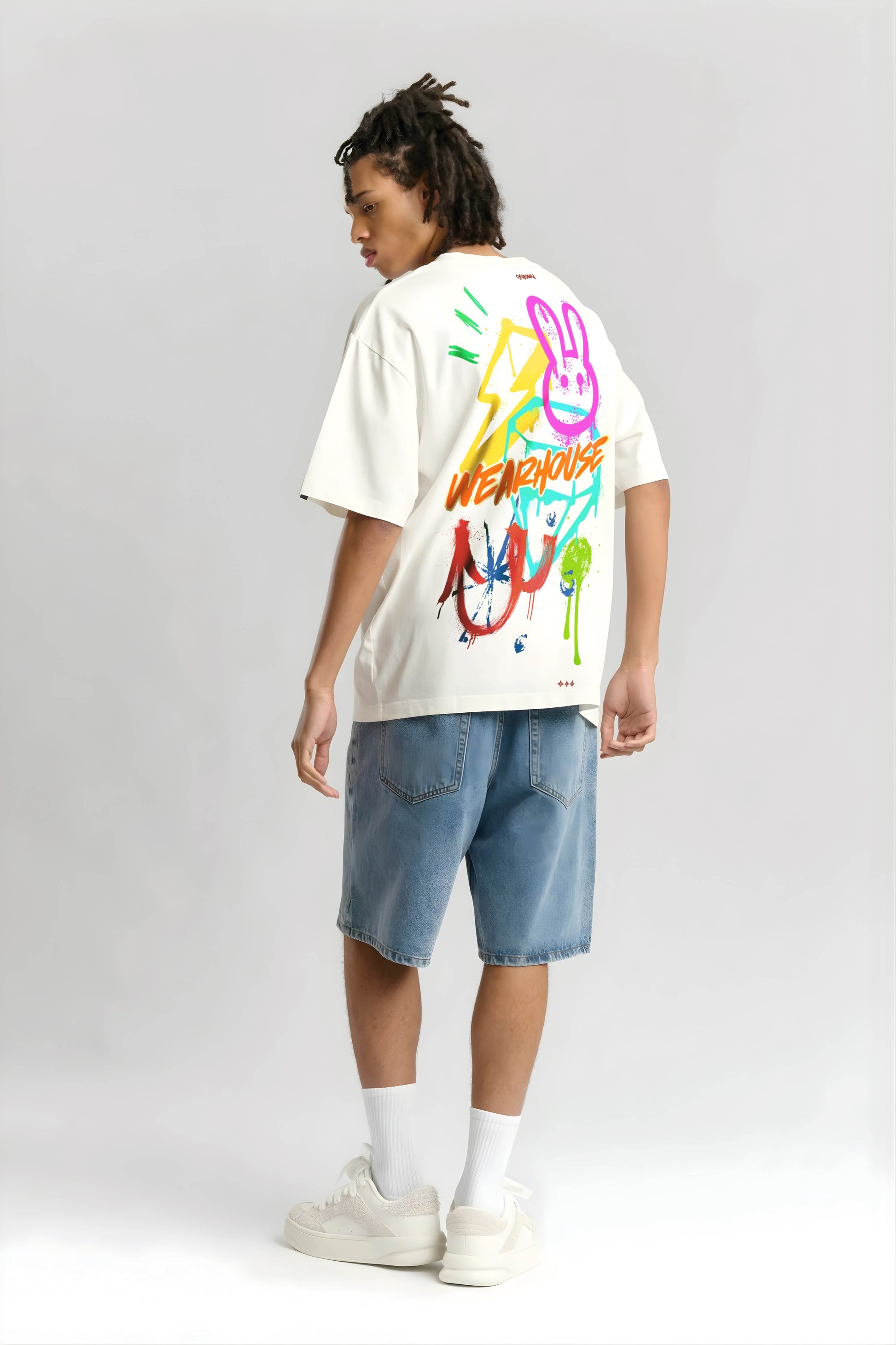 Person wearing an offwhite t-shirt with colorful graphics and text, standing against a plain background
