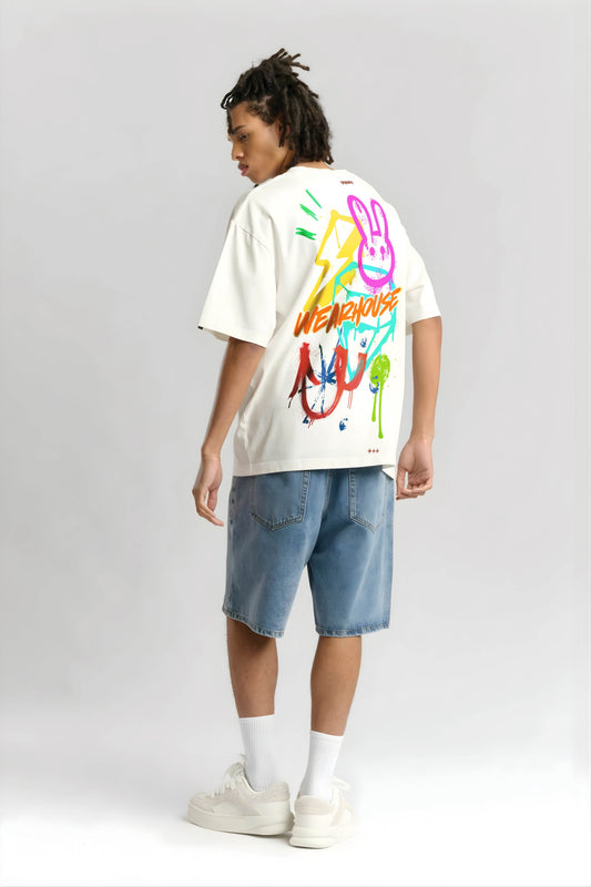 Person wearing an offwhite t-shirt with colorful graphics and text, standing against a plain background