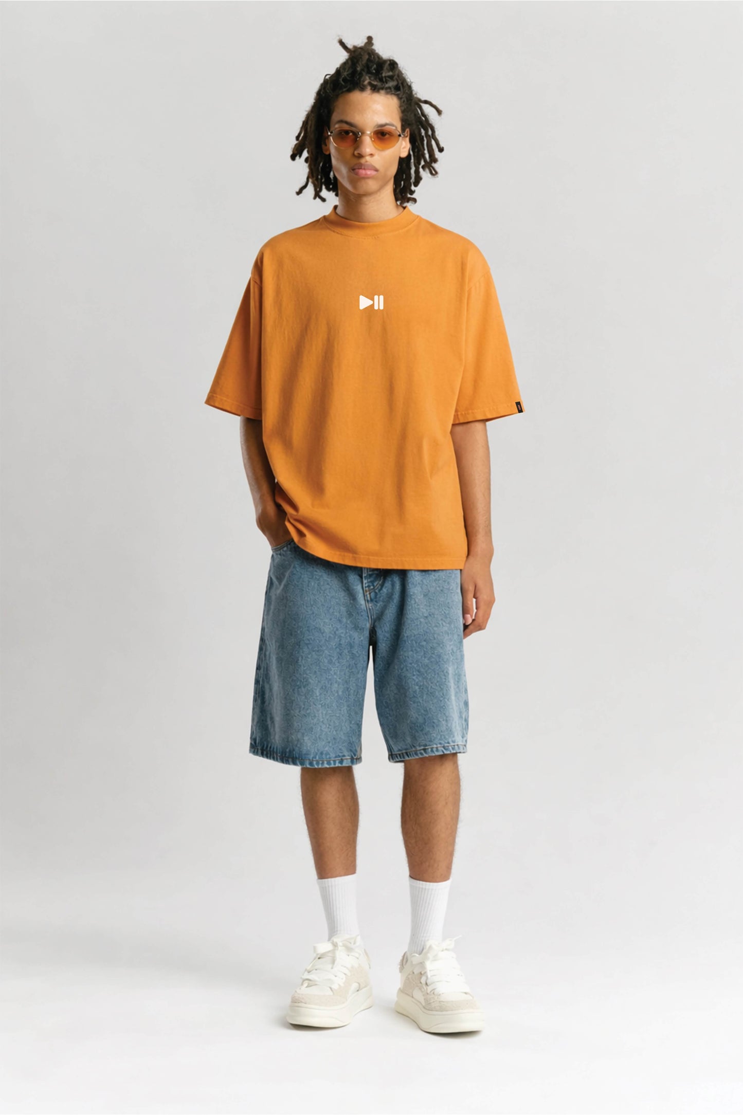 Person wearing an orange t-shirt with a logo and blue shorts on a white background