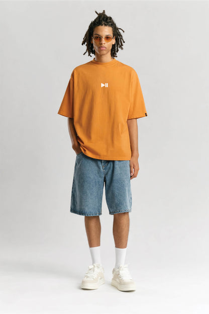 Person wearing an orange t-shirt with a logo and blue shorts on a white background