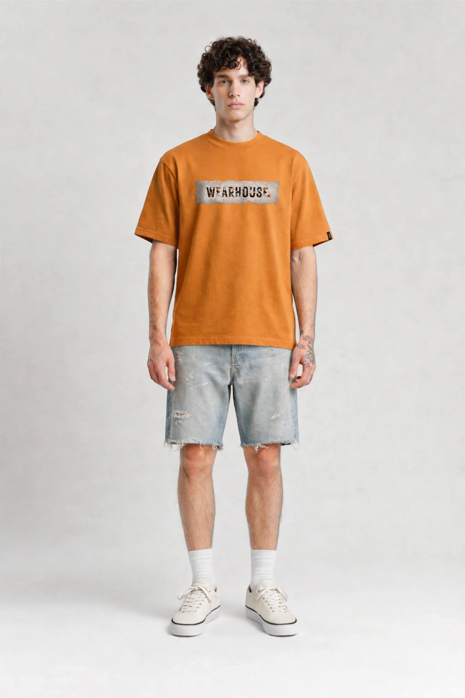 Person wearing an orange t-shirt with a logo and light gray shorts on a white background