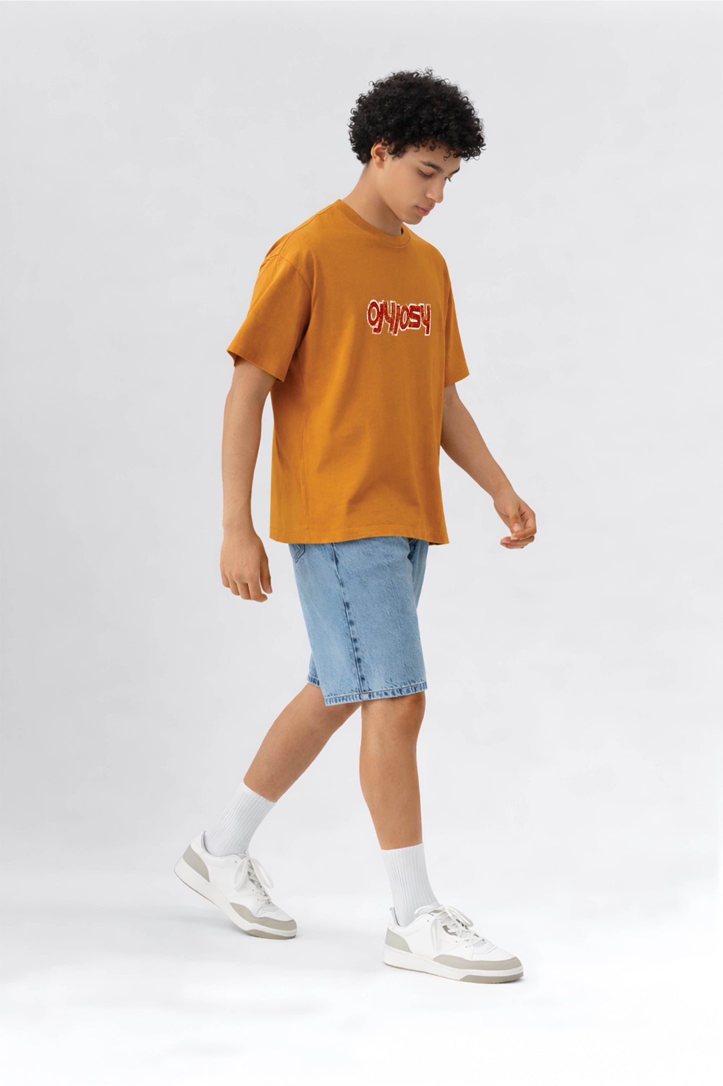 Person wearing an orange t-shirt with text and blue shorts on a white background